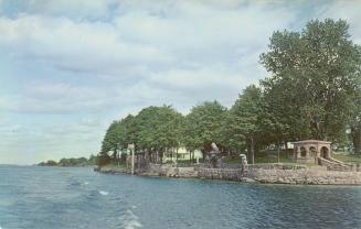 Colorized photograph of an island with a big house and boat house built on it in the middle of  ...