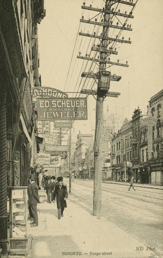 Sepia-toned postcard depicting a view of Yonge Street from the sidewalk with hydro poles and po ...