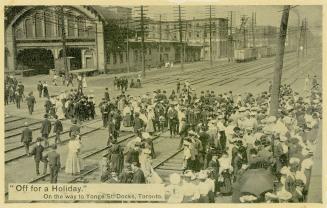 Black and white photo postcard depicting a crowd of people lined up to buy tickets for and cros ...