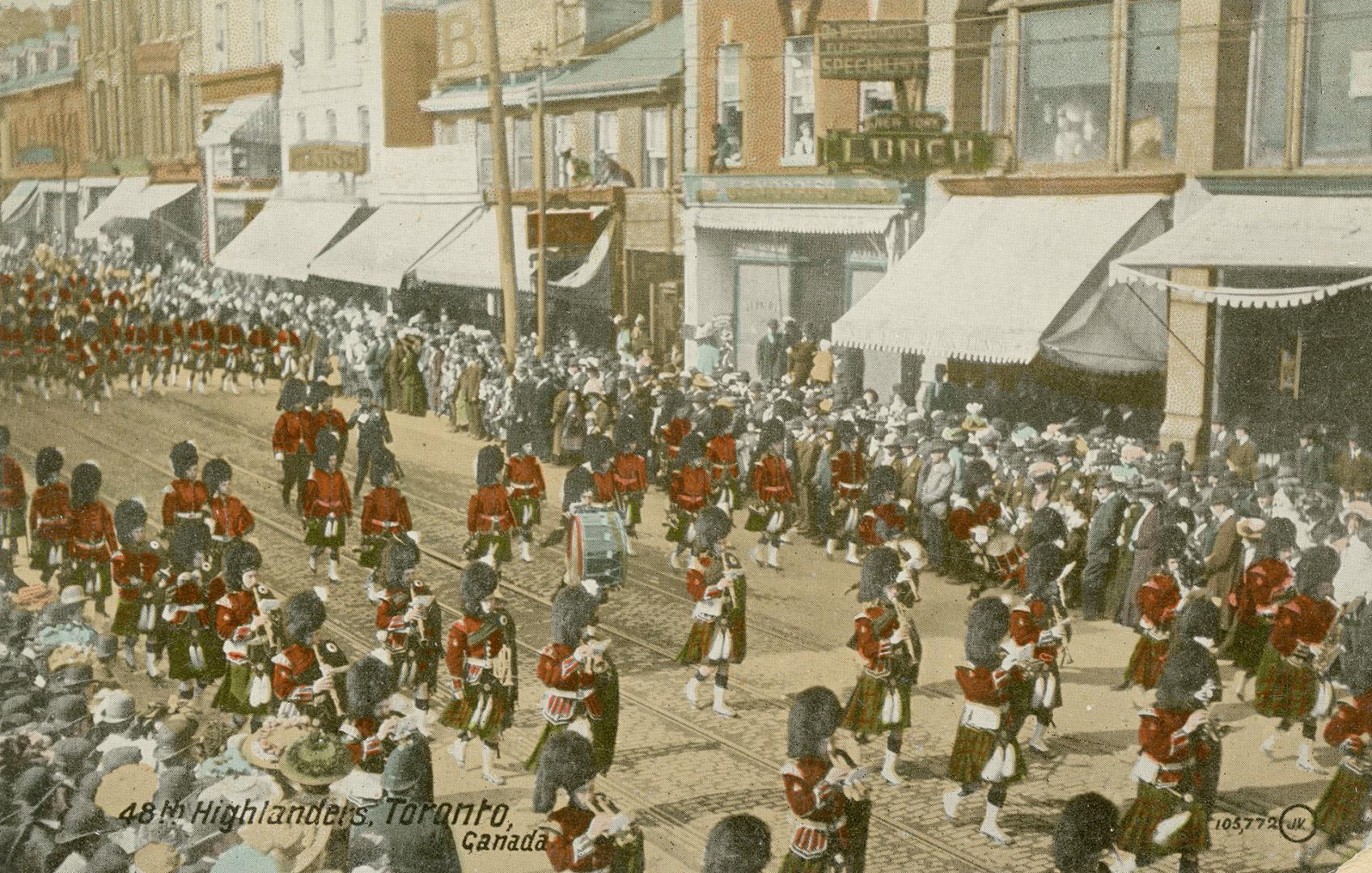Colour postcard depicting a parade procession of men in red army attire and bearskin hats with  ...