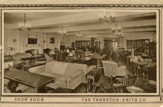 Sepia-toned photo postcard depicting an interior view of a furniture store, showing various sof ...