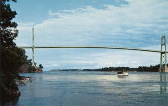 Color photograph of a bridge spanning a river with a boat running underneath it.