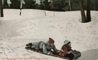 Colorized photograph of a boy and a girl tobogganing down a hill.