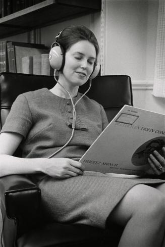 A woman sits in a chair listening to a record using headphones. 
