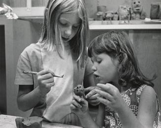 Two girls at a table making an object out of clay. 