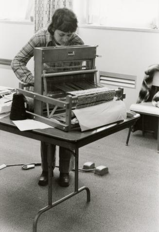 Picture of a woman weaving on a small loom. 