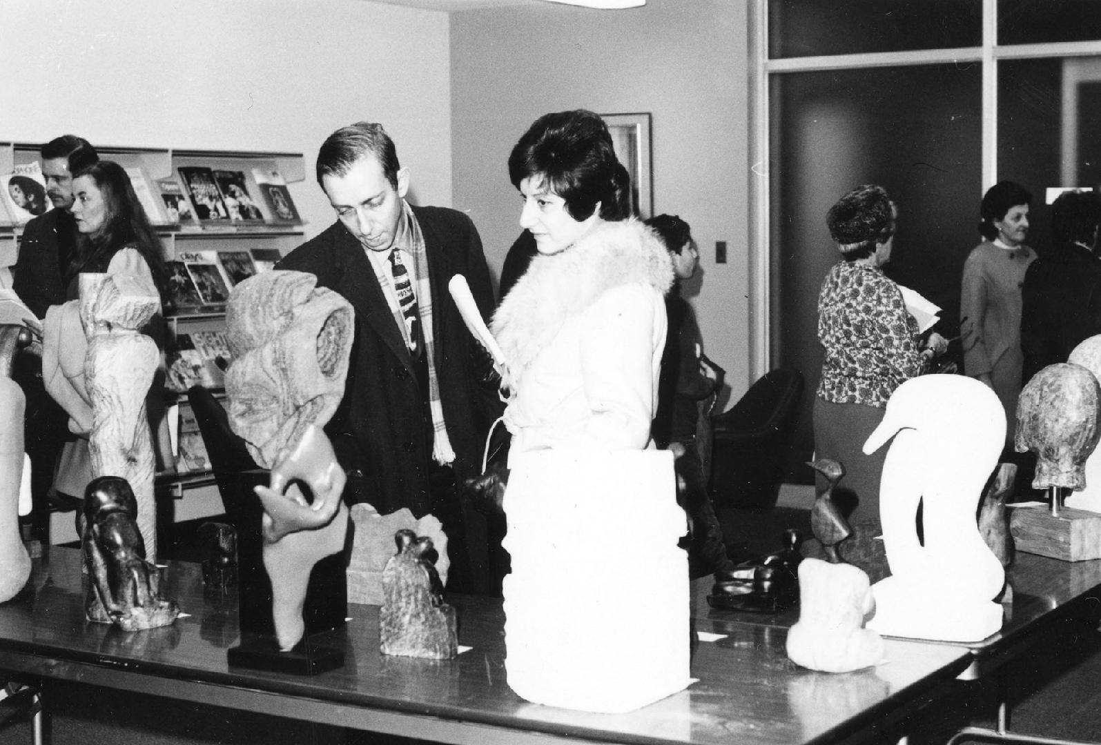 People in a room looking at sculptures on display on tables. 