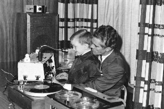 Picture of a man with a boy in his lap showing him how to use recording equipment. 