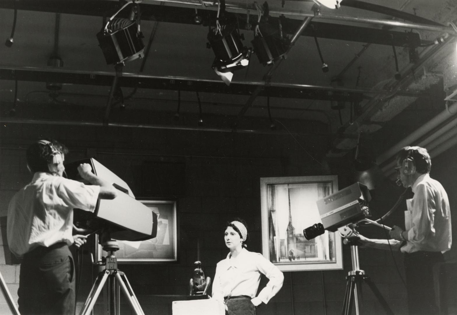 Picture of two people using television cameras to film a woman talking. 