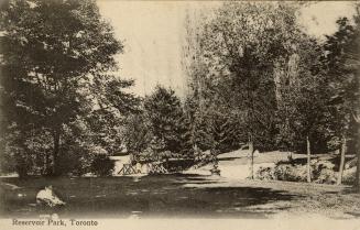 Black and white photograph of a wooded area with people relaxing. Wooden bridge is on the left.