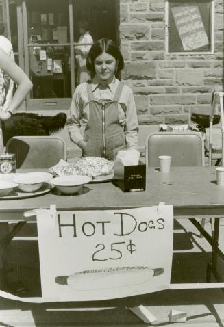 Picture of a girl at a hotdog stand with sign saying 25 cents. 