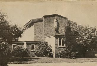 Black and white photo postcard depicting the front of a church with a statue of a saint and a c ...