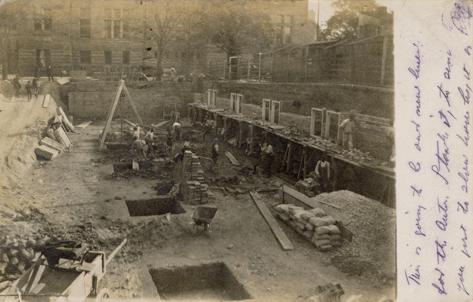 Black and white photograph of a work crew taking wheel barrows of debris away from a demolished ...