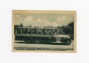 Black and white photograph of long bus coach with passengers inside.