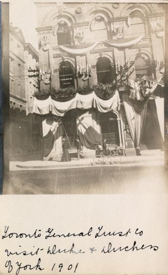 Black and white photograph of the front entrance of a public building. The door is festooned wi…