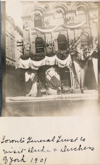 Black and white photograph of the front entrance of a public building. The door is festooned wi ...