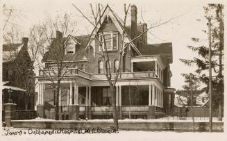 Black and white photograph of a large house with a wrap around porch.