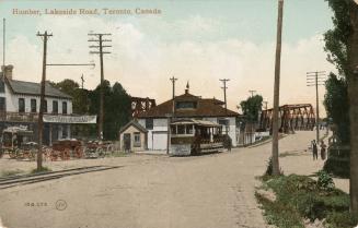 Colorized photograph of a streetcar traveling along track in front of a two story house. 