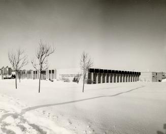 Picture of large one storey library administration building with snow on front lawn. 