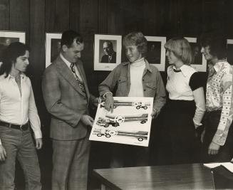 Picture a student showing a picture of bookmobile trucks to a man and three other students. 