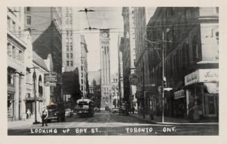 Black and white photograph of a city street with skyscrapers on either side and a clock tower a ...