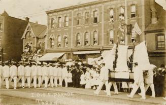 Black and white photograph of a city street with men in white uniforms marching.