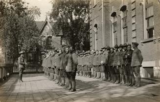 Black and white photograph of soldiers lined up for role call in front of a collegiate building ...