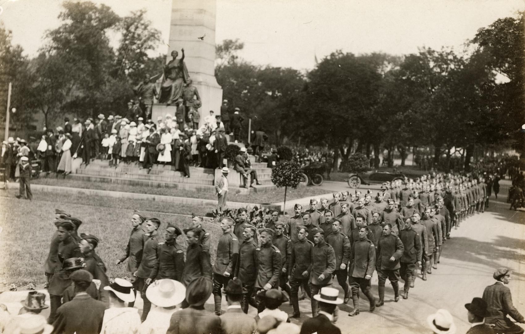 Black and white photograph of marching in front of a stone monument.