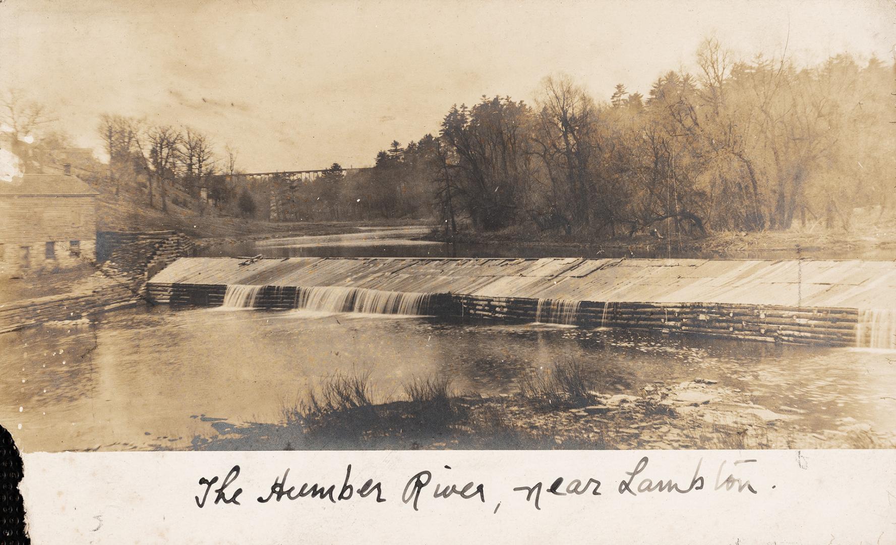 Black and white photograph of a river running over a log wall.