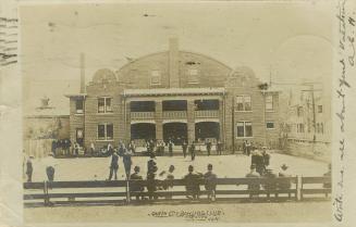 Black and white photograph of a three story brick building with balconies in the middle.