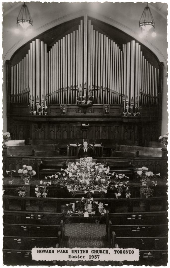 Black and white photo postcard depicting the interior of a church with a minister standing at t ...