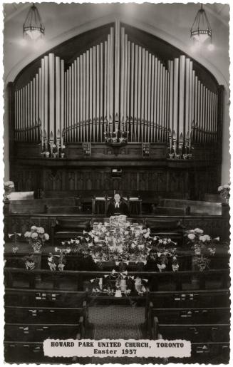 Black and white photo postcard depicting the interior of a church with a minister standing at t ...