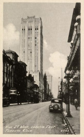 Black and white photo postcard of King Street looking east with a car and shops in view. A shop ...