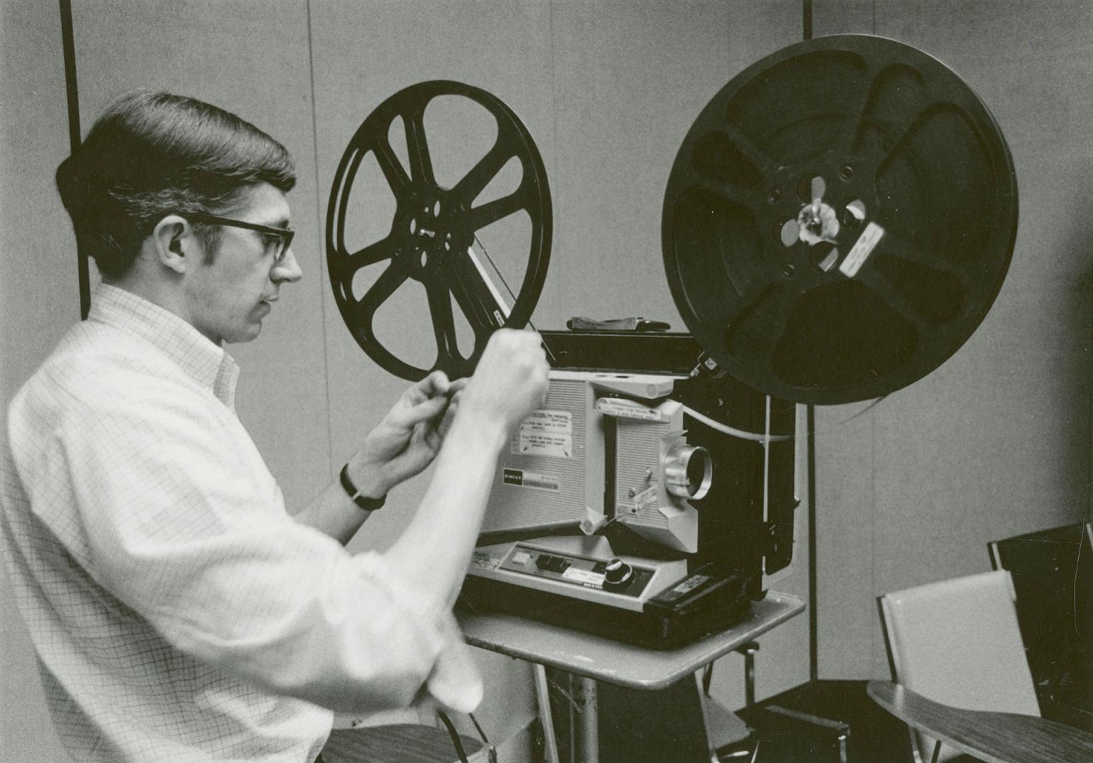 Picture of man loading a film onto a projector. 