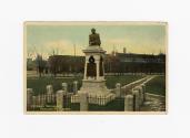 Colour photo postcard depicting a monument with a bust at the top, surrounded by a fenced-off a ...