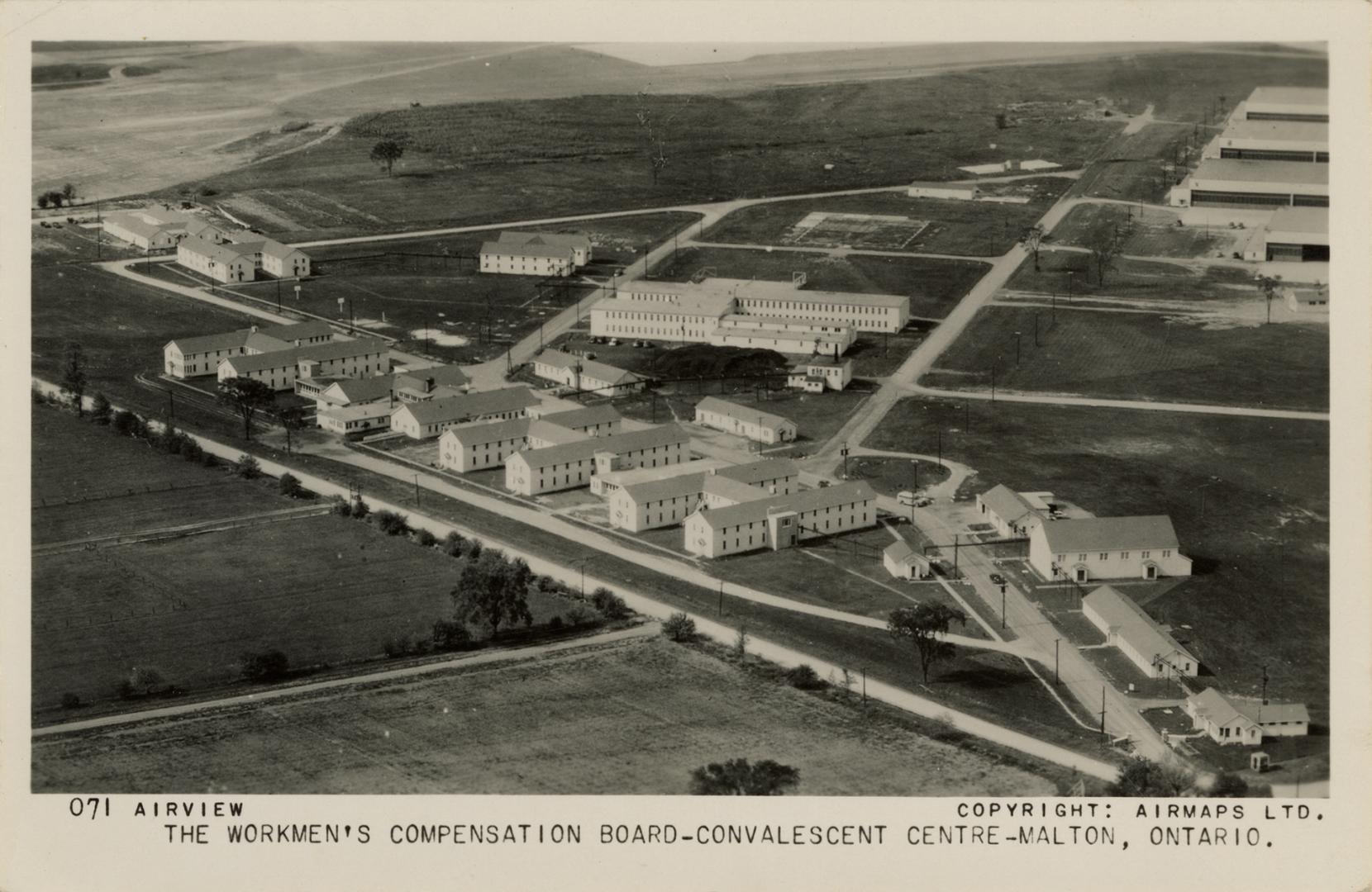 Black and white photo postcard depicting an aerial view of several two-story row buildings in a ...