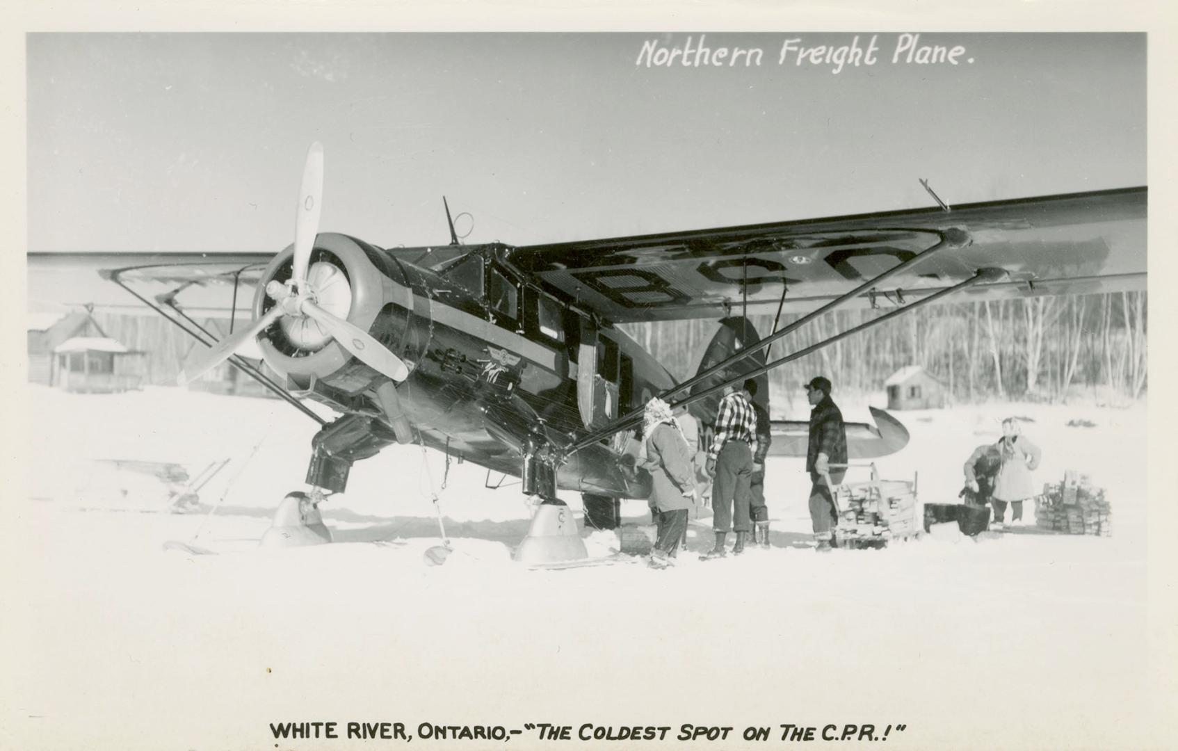 Black and white photograph of people loading a small plane in the wintertime.