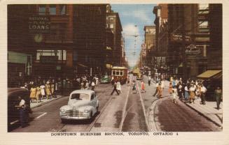 Colour postcard depicting a downtown street with a streetcar, cars, and pedestrians on the side…