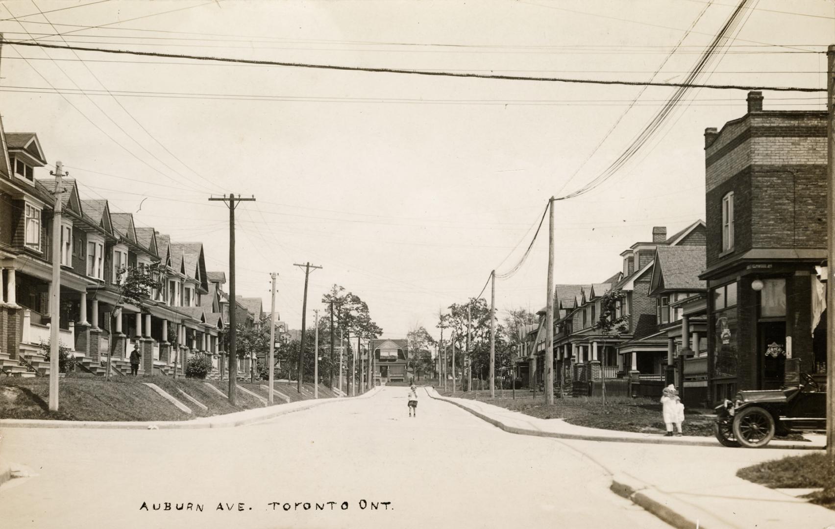 Black and white photo postcard depicting a view looking down a street with a child standing in  ...