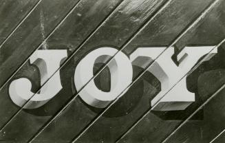 Black and white photograph of the letters JOY painted on a wooden background.