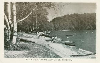 Black and white photograph of a people and canoes on the shoreline of a lake.