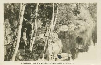 Black and white photograph of a woman sitting on a rocky ledge beside a still body of water.