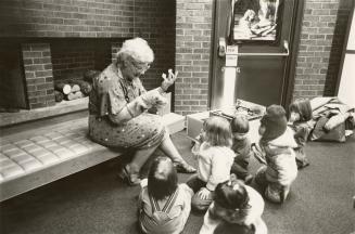 Picture of a librarian telling a story with puppets to children seated on floor. 