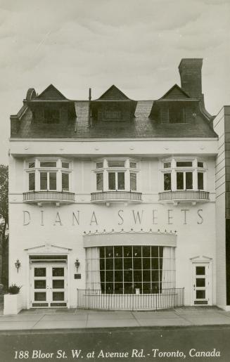 Black and white photo postcard depicting the exterior frontage of a two-story business with the ...