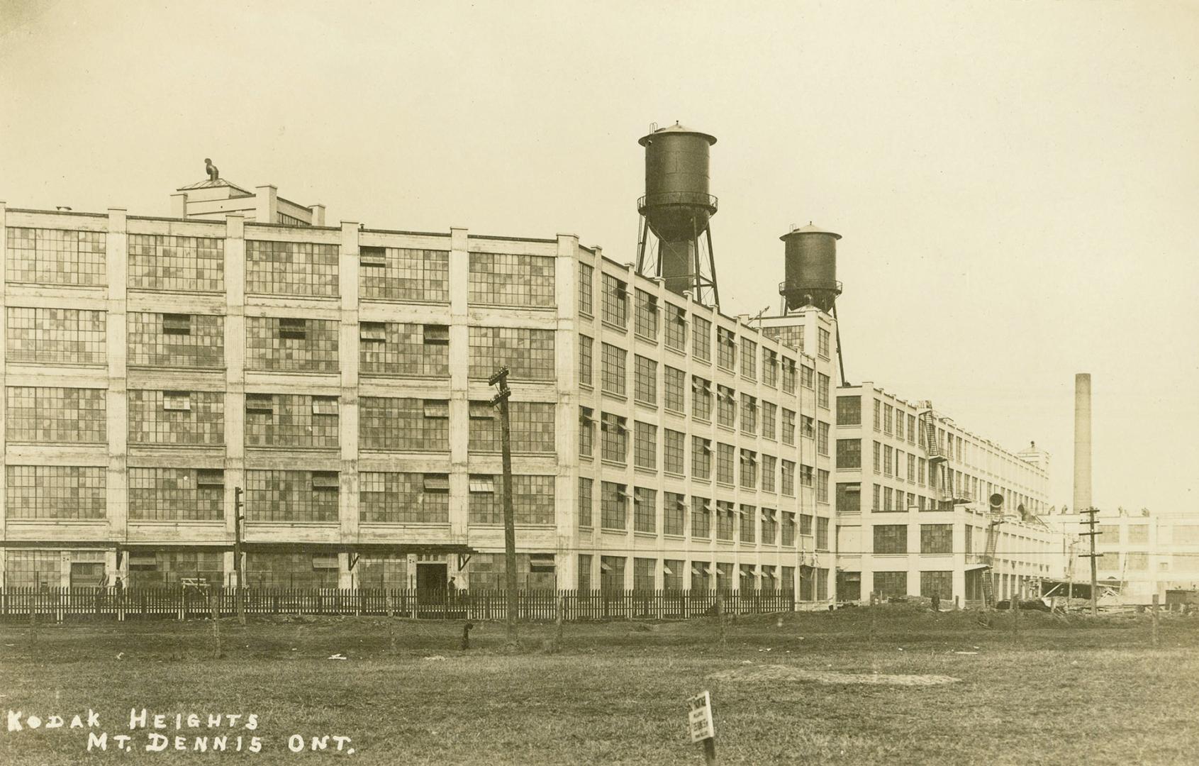 Black and white photo postcard depicting the exterior of two large five-story buildings surroun ...