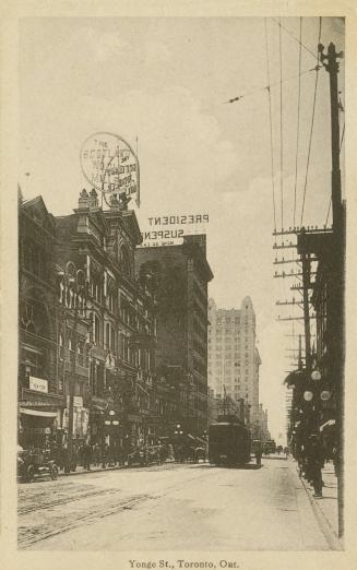 Black and white photo postcard depicting a view of Yonge St. with some buildings, retail shops, ...