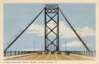 Colorized photograph looking directly across a long suspension bridge. Five automobiles are dri ...