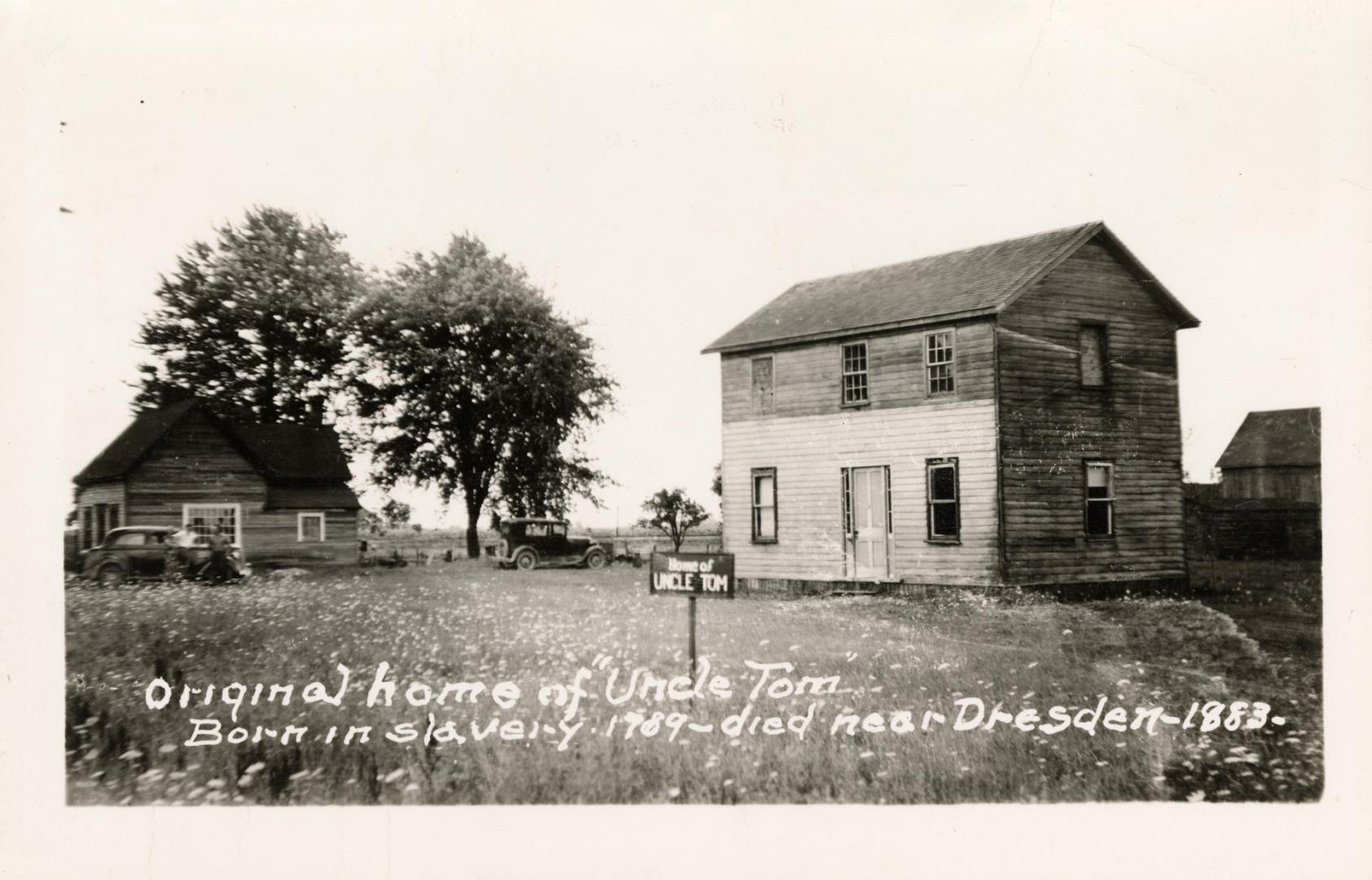 Black and white photograph of a two story frame house with automobiles in front of it.