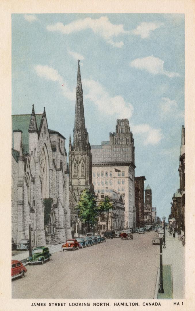 Colorized photograph city street with parked cars lining it. Churches are on the left hand side ...