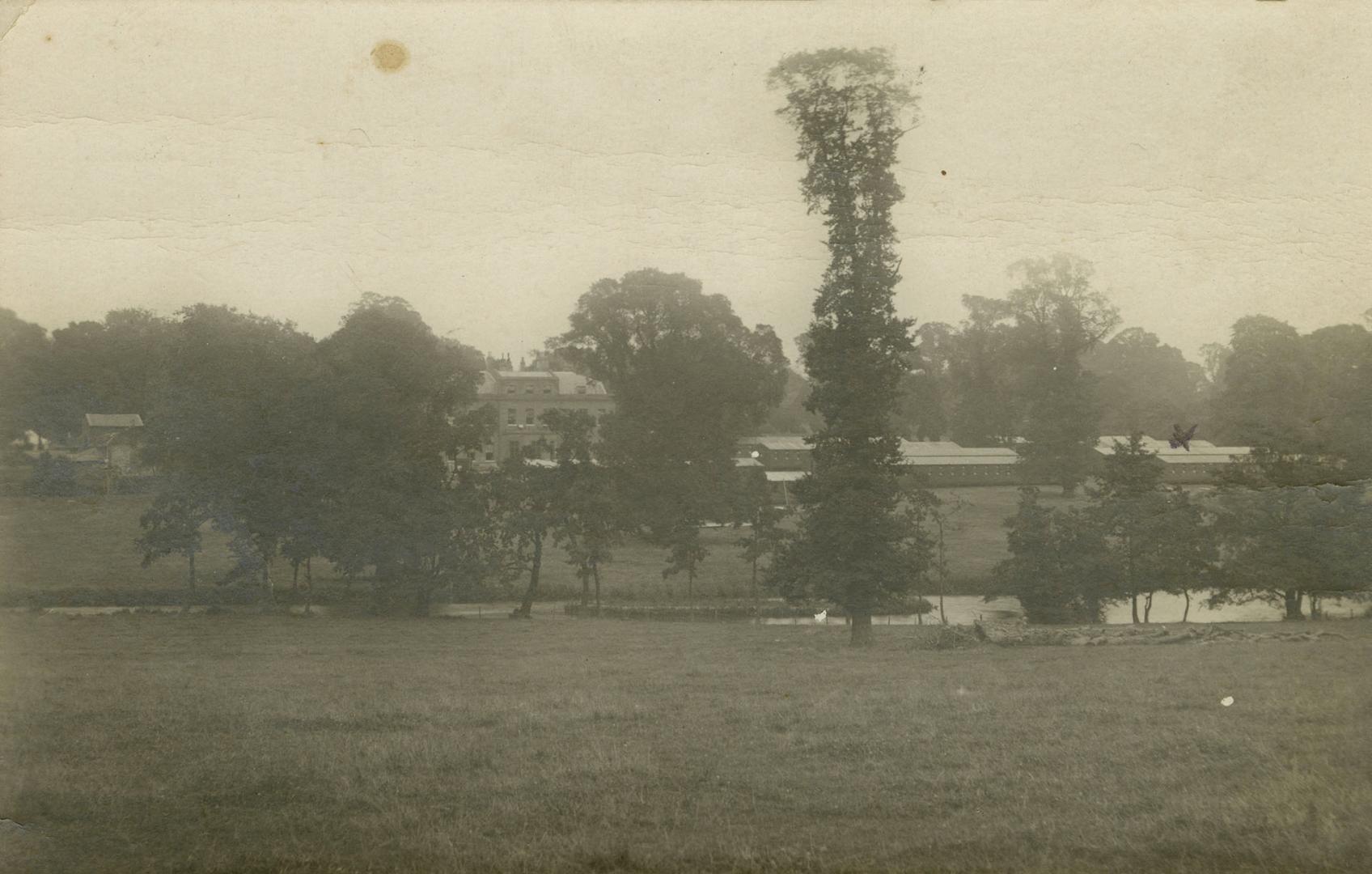 Black and white photograph of a large public building surrounded by water, trees and smaller bu ...